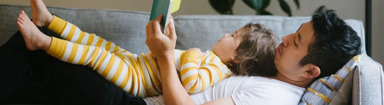 baby lying in father's arms reading a book